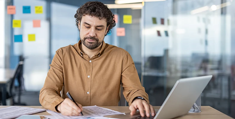 Professional software engineer working at a desk with a laptop and documents in a modern office